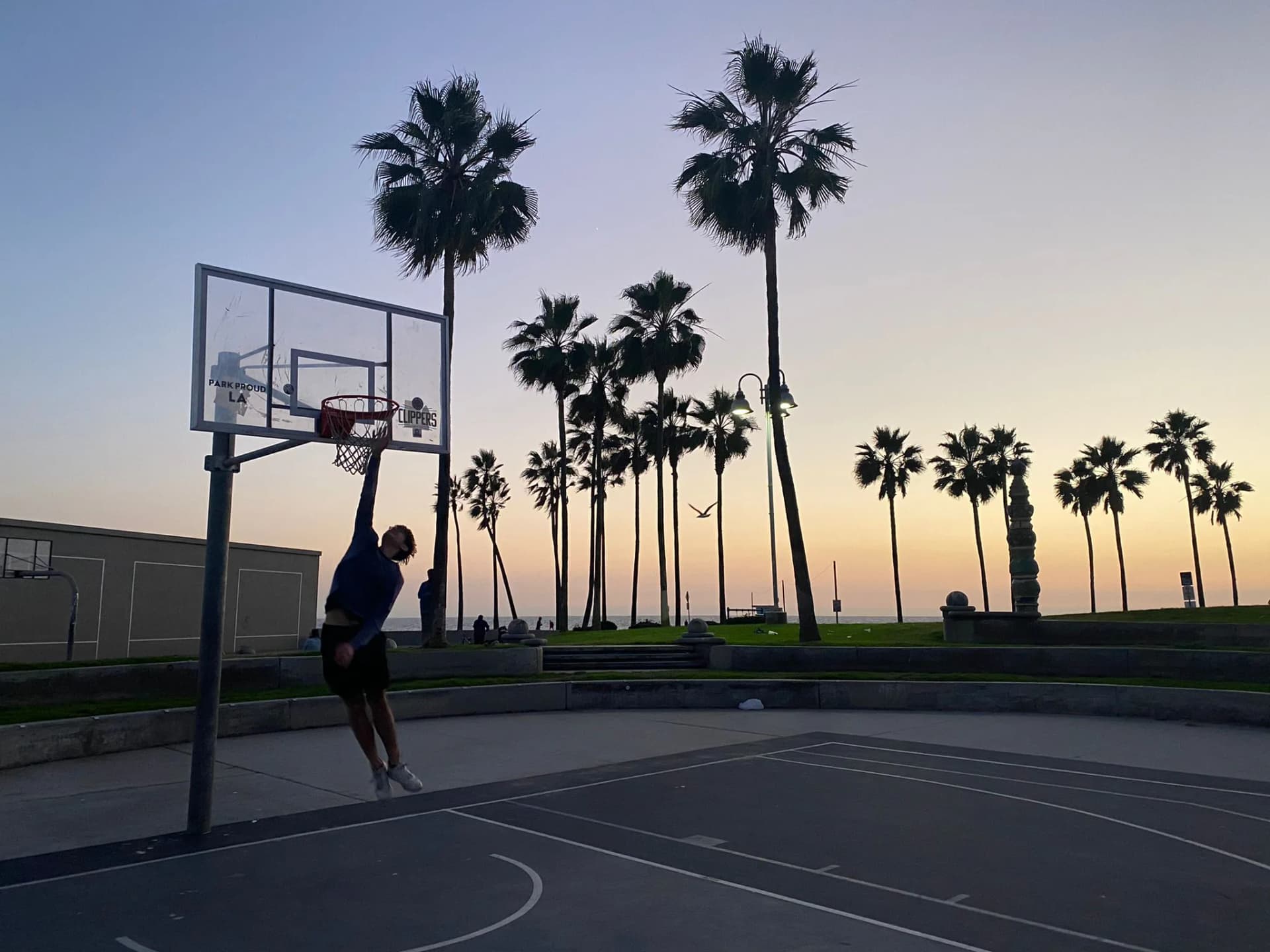 Ragazzo gioca a basket in un campo all’aperto con palme al tramonto, esempio di sport e tempo libero durante un anno all’estero in USA nel sistema scolastico americano.